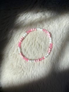 a pink and white beaded bracelet sitting on top of a fur covered bed next to a window