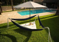 an umbrella and hammock set up in the grass next to a swimming pool