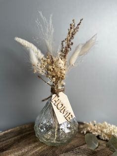 a glass vase with dried flowers in it and a tag that says home on it