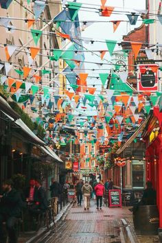 many people are walking down the street with colorful flags hanging from the wires above them