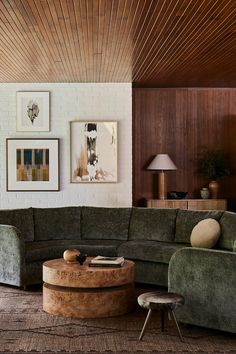 a living room with green couches and pictures on the wall above them, along with a round coffee table