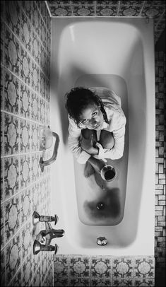 a woman sitting in a bathtub with her hands on the water and looking at the camera