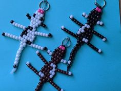 two beaded keychains are sitting on a blue surface, one has pink and white beads in the shape of people