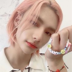 a young man with pink hair wearing a white shirt and smiling face beaded bracelets