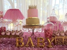 a table topped with pink and gold baby shower items next to a cake covered in icing