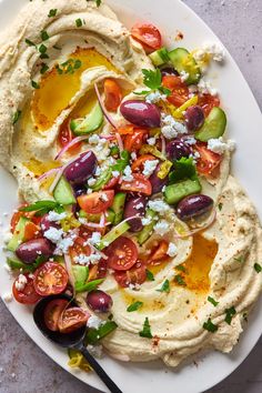 hummus with olives, tomatoes, cucumbers and feta cheese on a white plate