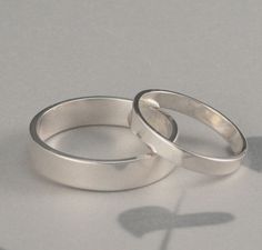 two silver wedding rings sitting on top of a white table next to a shadow of a flower