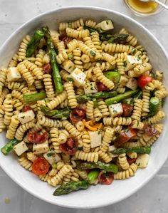 pasta salad with asparagus, tomatoes and feta cheese in a white bowl