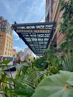 a sign that reads chelsea market hanging from the side of a building with lots of greenery