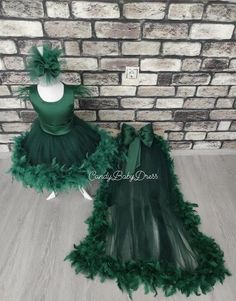 two green dresses are on display in front of a brick wall, one is made from tulle and the other has feathers