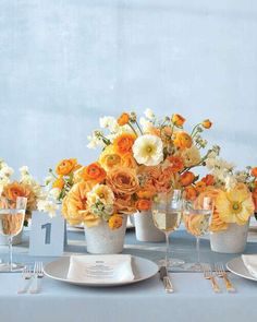 an arrangement of orange and white flowers in vases on a table with silverware