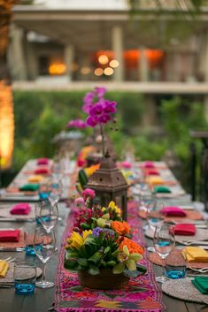 the table is set with colorful flowers and place settings for guests to sit down at