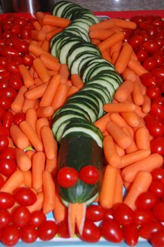 a platter with carrots, cucumbers and tomatoes arranged in the shape of a snake