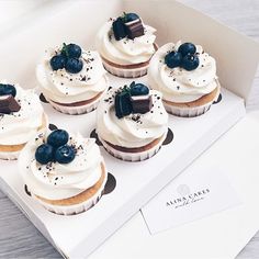 six cupcakes with white frosting and blueberries on top in a box