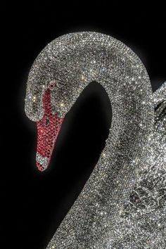 a close up of a swan made out of silver sparkles and red beads on a black background