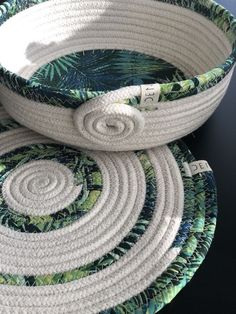 two woven baskets are stacked on top of each other, one has a white rope and the other is blue with green leaves