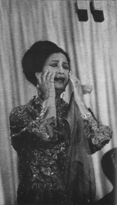 a woman talking on a cell phone while standing in front of a curtain with her hands to her face