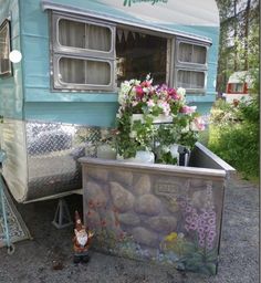 an old camper with flowers in the window and a potted plant next to it