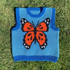 a blue sweater with an orange butterfly on it sitting in the middle of some grass