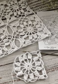 two crocheted doily sitting on top of a wooden table next to a piece of paper