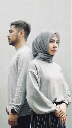 a man and woman standing next to each other in front of a white wall with their hands behind their backs