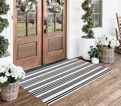 the front door is decorated with wreaths and potted plants on the wooden porch