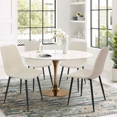 a dining room table with white chairs and a blue rug in front of the window