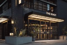 the knott hotel is lit up at night, with plants in pots on the sidewalk