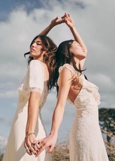 two women standing next to each other in front of the ocean with their hands together