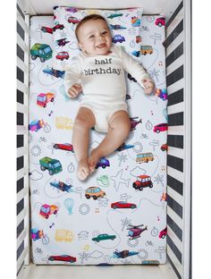 a baby laying in a crib with cars and trucks on it