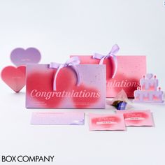 some pink and purple greeting cards are on the table next to two boxes with hearts