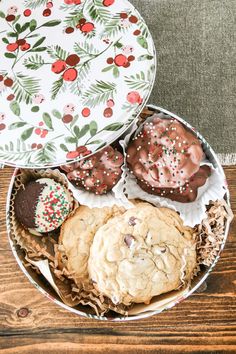 an assortment of cookies and pastries in a tin on top of a wooden table