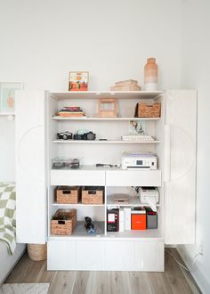 a white book shelf filled with books on top of a hard wood floor next to a bed