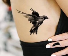 a black bird tattoo on the side of a woman's stomach, with white nails