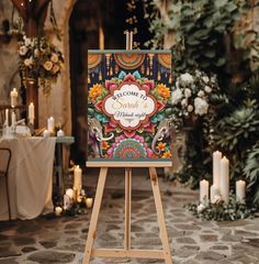 an easel stands in front of a decorated table with candles and flowers on it