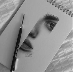 a black and white photo of a woman's face next to a pen on top of a notebook