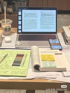 an open laptop computer sitting on top of a wooden table next to books and papers