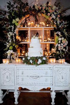 a wedding cake on top of a white table with candles and flowers in the background