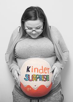 a pregnant woman holding her stomach with the words kinder surprise painted on its belly