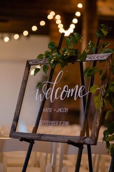 a welcome sign sitting on top of a wooden easel next to a table with white chairs