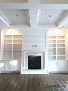 an empty living room with white bookcases and fireplace in the center is lit by recessed lights