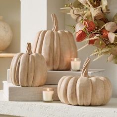 three white pumpkins sitting on top of a shelf next to some flowers and candles