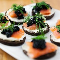 small appetizers with smoked salmon and black cavias on them are arranged on a white platter