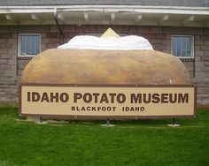 a large potato sitting on top of a field next to a sign that says idaho potato museum