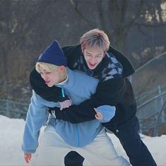 two young men are playing in the snow on their skateboards and one is holding his arm around the other