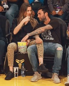 a man and woman sitting next to each other in front of a crowd at a basketball game