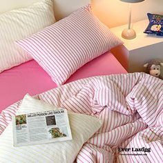 a bed with pink and white sheets, pillows and a stuffed animal on the nightstand