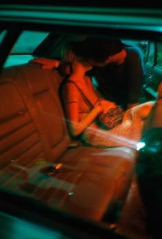 a man and woman sitting in the back seat of a car, looking at their cell phones