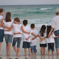 a group of people standing on top of a sandy beach next to the ocean with their arms around each other