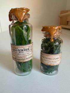 two glass jars filled with green vegetables on top of a table next to each other